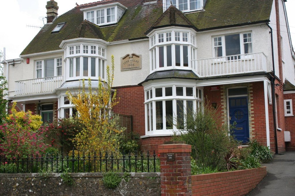 Red brick home with white bay windows behind a colourful front garden